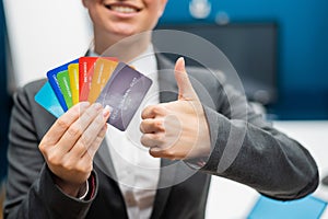 Business woman in a suit holds a lot of different credit cards and shows a thumb up.