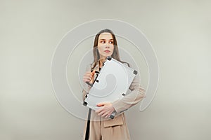 Business woman in a suit with a metal case in her hands stands on a beige background and looks away with a surprised face