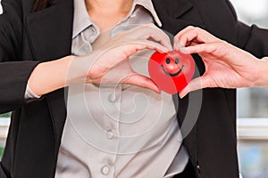 Business woman in suit standing holding red heart and making heart shape by hands indoor on city background