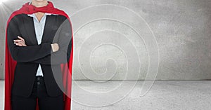 Business woman superhero with arms folded against grey wall with flare