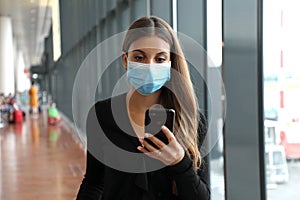 Business woman with surgical mask and mobile phone looks for flight at the airport