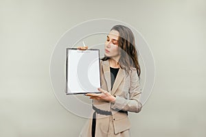 Business woman with a tablet in her hands stands on a beige background looks at a blank white sheet of paper and shows a pen on