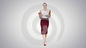 Business woman with tablet walking and talking to the camera on gradient background.