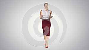 Business woman with tablet walking and talking to the camera on gradient background.