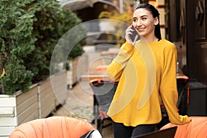 Business woman talking on a cell phone, standing at the table of a street cafe, a brunette girl smiles and talks to a