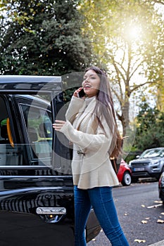 Business woman talking on her mobile phone whilst steps into a black taxi