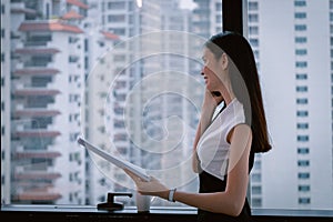 Business Woman talking with mobile phone  in Modern office building and looking documents in another hand with city in background