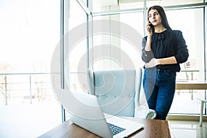 Business woman talking at phone near the table and looking at window