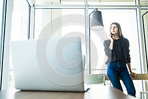 Business woman talking at phone near the table and looking at window in office