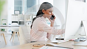 Business woman talking on a phone while working on a computer in an office. Dedicated and happy young professional