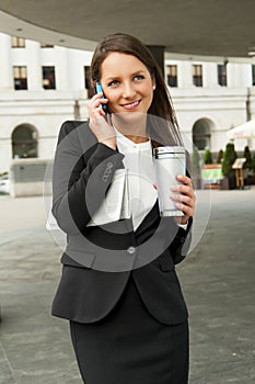 Business woman talking by smartphone, with caffee cup and newspap