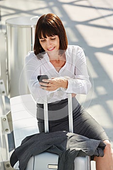 Business woman traveler waiting with phone and suitcase