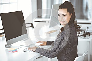 Business woman using computer at workplace in modern office. Brunette secretary or female lawyer smiling and looks happy