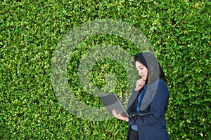 Business woman using laptop computer with green tree wall background, great for your design or text, asian