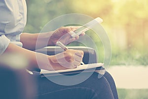 Business woman using mobile smart phone and writing on notebook