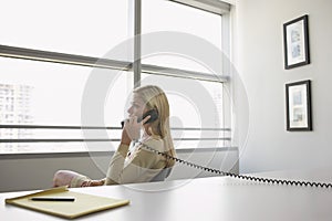 Business woman using phone sitting at office desk side view