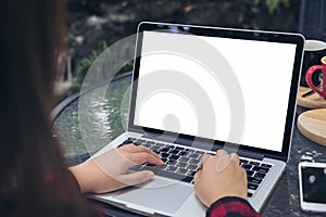 Business woman using and typing on laptop with blank white screen , smart phone and coffee cups on glass table