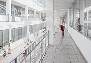 Business Woman Walking Along the Office Corridor. Smiling Businesswoman Goes Against White Offices Background. A young pretty girl