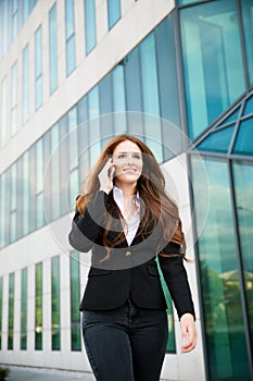 Business woman walks outdoor with smartphone talking to her team