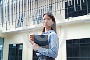 A business woman wearing a blue shirt and holding a cup of coffee and a tablet