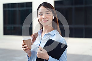 A business woman wearing a blue shirt and holding a cup of coffee and a tablet