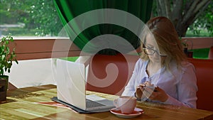 Business woman wearing glasses working in cafe and talking on smart phone