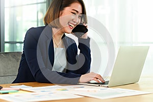 Business woman wearing a suit talking on the phone and using a laptop smiling face