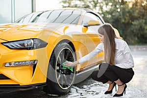 Business woman wearing on a white shirt and black trousers cleaning a wheel, car rims