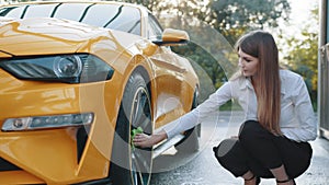 Business woman wearing on a white shirt and black trousers cleaning a wheel, car rims of modern luxury yellow sport car