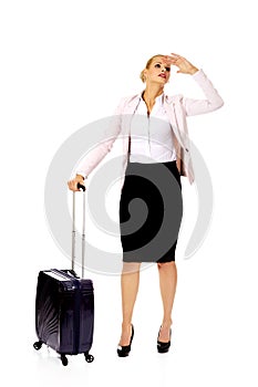 Business woman with wheeled suitcase covering eyes with hand