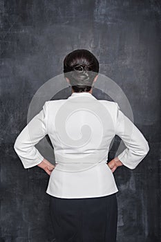 Business woman in white blazer standing back pose on blackboard background