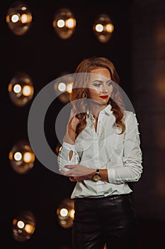 Business Woman in a white shirt against the background of burning lamps in the interior of a dark Studio.Model with long hair and