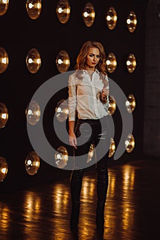 Business Woman in a white shirt against the background of burning lamps in the interior of a dark Studio.Model with long hair and