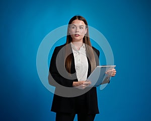 Business woman in white suit and black suit standing and holding clipboard by her hands, looking away, blue background