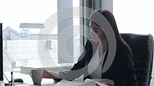 Business woman at the window, works with documents, working at the table in the office