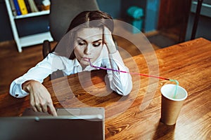 Business woman working laptop computer drinking coffee through straw. Busy young woman works at office workplace. Crisis