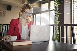 Business woman is working on laptop and drinking cup of coffee and glass of water in coffee shop, restaurant