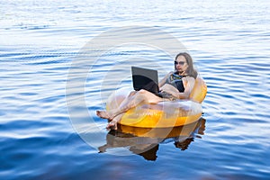 Business woman working on a laptop in an inflatable ring on the sea, the concept of working on vacation.