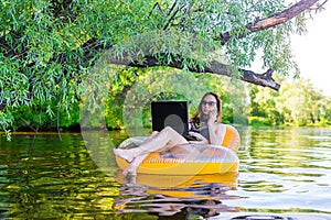 Business woman working on a laptop and talking on smartphone in an inflatable ring in the water, a copy of the free space.