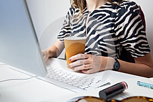 Business woman working in minimalistic office. Young female person with coffee in front of desktop computer at modern workplace