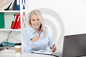 Business woman working in office with documents. Beautiful middle aged woman looking at camera with smile while siting