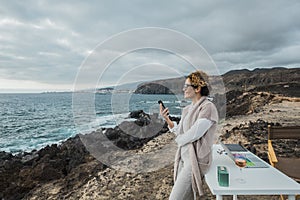 Business woman working outdoor in total freedom in front of the ocean with a desktop and notebook and mobile phone - concept of