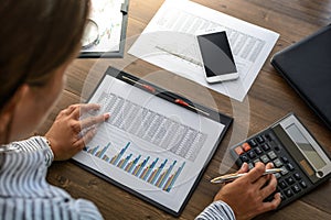 Business woman at workplace at wooden office table analyzes the data, schedules, prices, makes calculations on a calculator