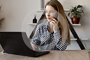 A business woman works in a home office while sitting at a laptop and talking on a cellphone. Internet technologies for