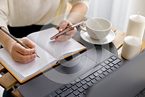 Business woman works at laptop, holds smartphone in her hand