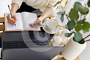 Business woman works at laptop, holds smartphone in her hand