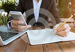 Business woman write on notebook and use cell phone working outdoor in coffee shop vintage tone