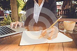 Business woman write on notebook and use laptop working outdoor in coffee shop vintage tone