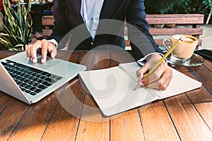 Business woman write on notebook and use laptop working outdoor in coffee shop vintage tone