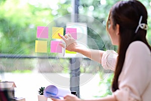 Businesswoman writing creative ideas on sticky notes on glass wall in modern office.